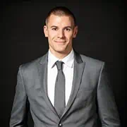 Professional businessman in gray suit smiling, standing confidently against a black background, representing corporate success and leadership.