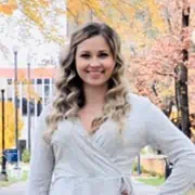 Alt text: Professional woman smiling outdoors with autumn trees, representing marketing success and business growth.
