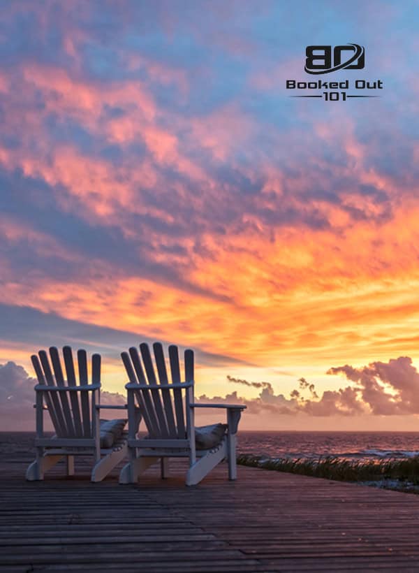 Sunset over the ocean with two Adirondack chairs on a wooden deck, highlighting tranquility, beach relaxation, and scenic coastal views.