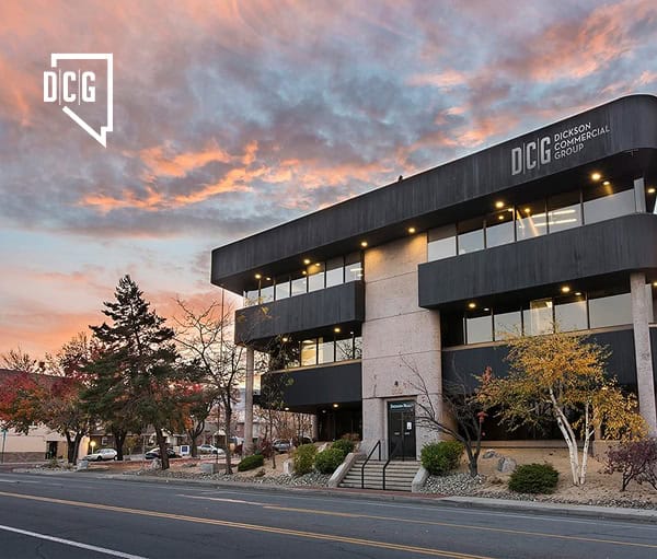Modern commercial office building with Dickinson Commercial Group signage, featuring sleek black exterior, large glass windows, and landscaped surroundings under a vibrant sunset sky.